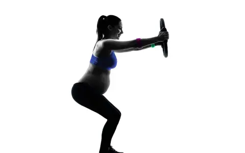 Gravid kvinna tränar med en pilatesring. Hon gör en knäböj och håller ringen framför sig med raka armar.