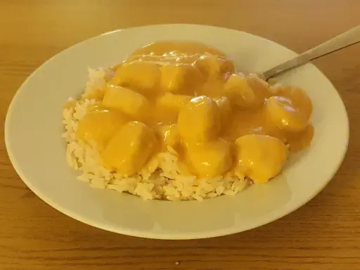 En tallrik med ris och krämiga fiskbullar i en gul sås. En nyttig och god måltid.