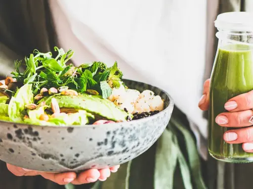 En person håller en skål med en hälsosam sallad och en grön smoothie. Perfekt mat att undvika gravid, med färska grönsaker och nötter.