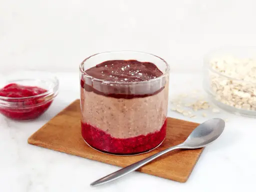 En glasburk med overnight oats propud choklad, hallonsylt och en sked.