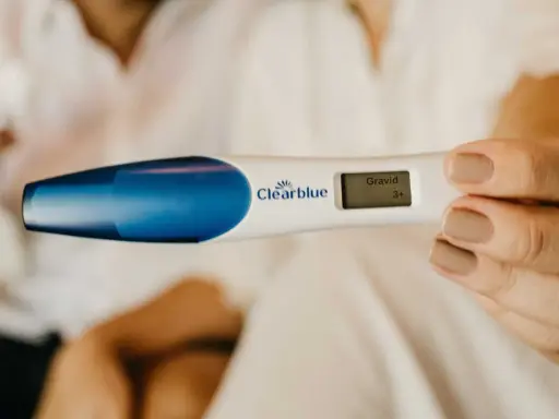 En hand håller ett digitalt graviditetstest som visar "Gravid 3+". En oväntad upptäckt, gravid utan att veta.
