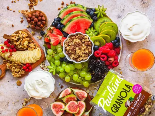 En lyxig frukostbricka med frukt, nötter, yoghurt och granola. Vattenmelon, kiwi, bär, vindruvor, banan och fikon skapar en färgsprakande och hälsosam start på dagen.