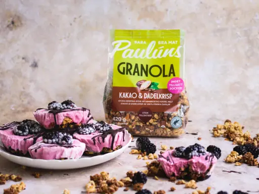 Rosa yoghurtglass med bär och granola, perfekt för ett snabbt yoghurtglass recept. Paulúns granola i bakgrunden.
