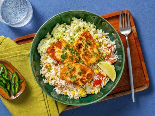 Grillad halloumi laktos serveras med ris, majs, tomat och kål. En limeklyfta och gröna paprikastrimlor fulländar rätten.