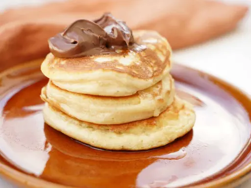 Amerikanska pannkakor med proteinpulver, toppade med chokladkräm, serveras på en brun tallrik. En hälsosam frukost!