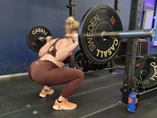 Kvinna utför en tung overhead squat med skivstång. Viktskivorna är märkta med "Casall Sweden".