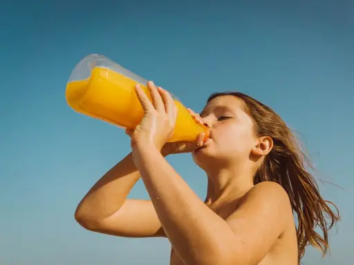 Barn dricker en stor flaska apelsinjuice, socker i juice ger energi på stranden.