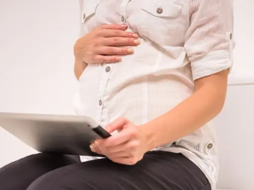 Gravid kvinna sitter på toaletten med en surfplatta, oroar sig för brun flytning.