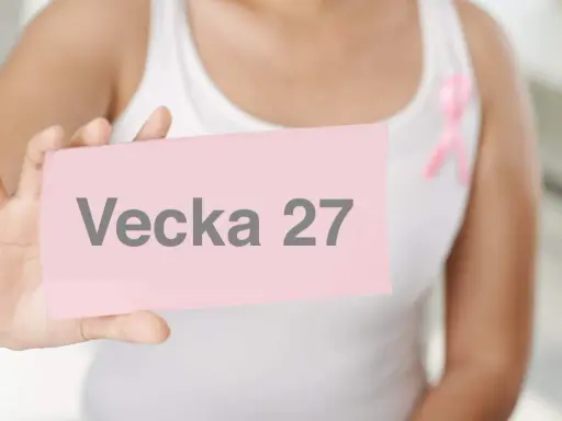 En person håller upp ett rosa kort med texten "Vecka 27". En rosa band pryder personens vita linne.