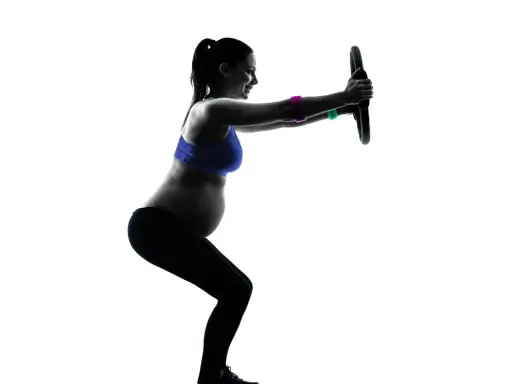 Gravid kvinna tränar med en pilatesring. Hon gör en knäböj och håller ringen framför sig med raka armar.