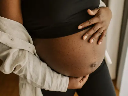 En gravid mage i tredje trimestern, varsamt omfamnad av händer. En ljus skjorta draperad över axeln.