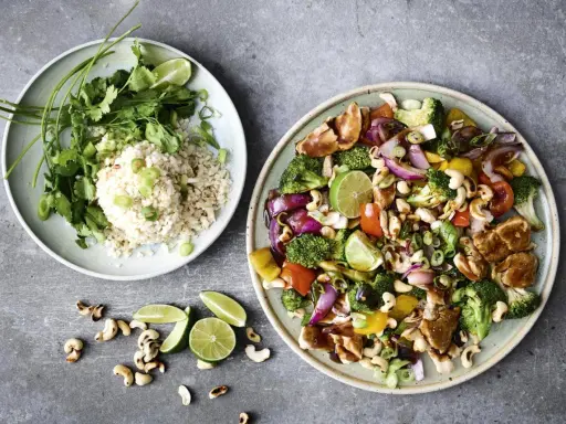 Två tallrikar med nyttig fredagsmat: ris med koriander och grönsaker med kyckling, cashewnötter och lime.