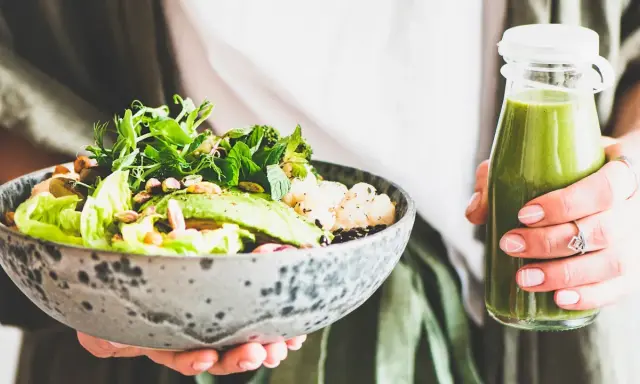 En person håller en skål med en hälsosam sallad och en grön smoothie. Perfekt mat att undvika gravid, med färska grönsaker och nötter.