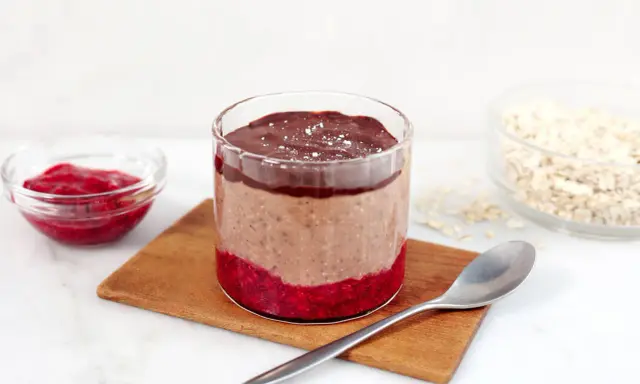 En glasburk med overnight oats propud choklad, hallonsylt och en sked.