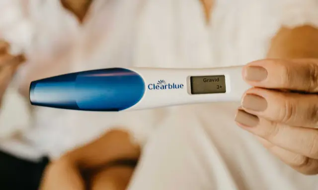 En hand håller ett digitalt graviditetstest som visar "Gravid 3+". En oväntad upptäckt, gravid utan att veta.