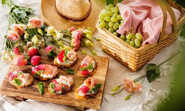 En härlig picknick med bruschetta toppad med jordgubbar och parmaskinka, färska vindruvor i korg och blommor.