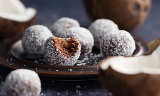 Chokladbollar med proteinpulver, rullade i kokos. En är uppäten, vilket avslöjar den mörka, saftiga insidan.