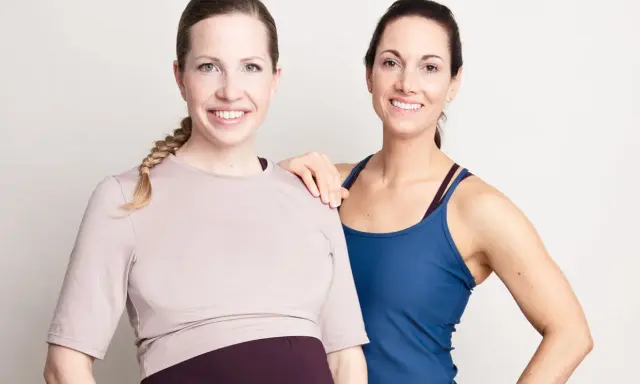 Två glada kvinnor, en gravid, poserar. De är klädda i träningskläder och ser ut att vara redo att lyfta tungt, gravid eller ej.