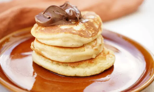 Amerikanska pannkakor med proteinpulver, toppade med chokladkräm, serveras på en brun tallrik. En hälsosam frukost!
