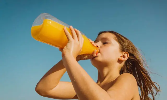 Barn dricker en stor flaska apelsinjuice, socker i juice ger energi på stranden.