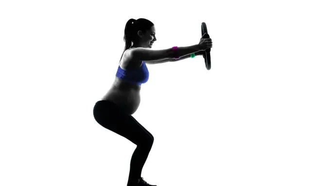 Gravid kvinna tränar med en pilatesring. Hon gör en knäböj och håller ringen framför sig med raka armar.