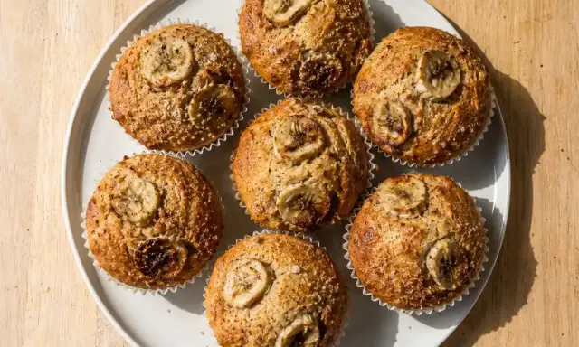 Sju gyllene bananmuffins med skivor av banan på toppen, redo att avnjutas. Ett perfekt bananmuffins recept för fika.