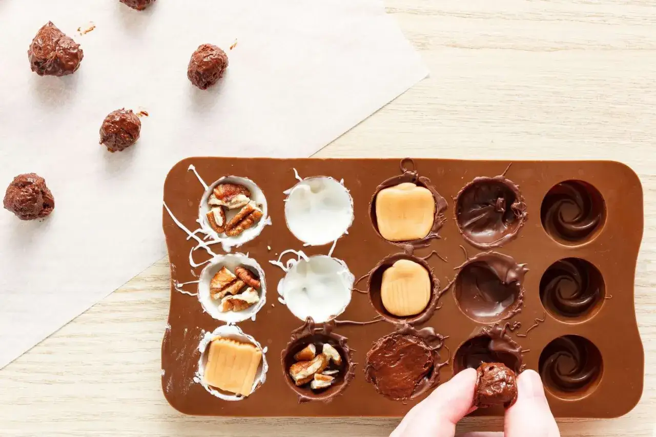 Gör snabbt chokladgodis med nötter och kola i en silikonform. En hand håller ett färdigt chokladtryffel.