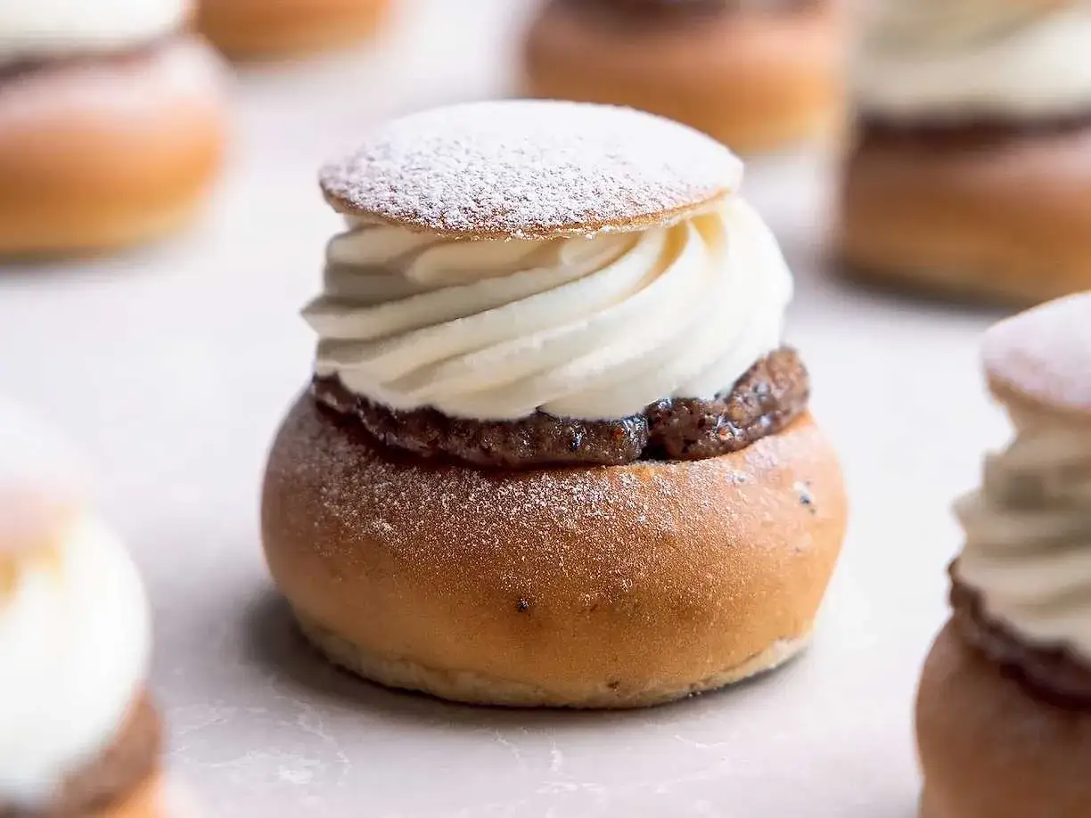 En n&auml;rbild av en nyttig semla med fluffig gr&auml;dde och mandelmassa, pudrad med florsocker. Flera semlor i bakgrunden.