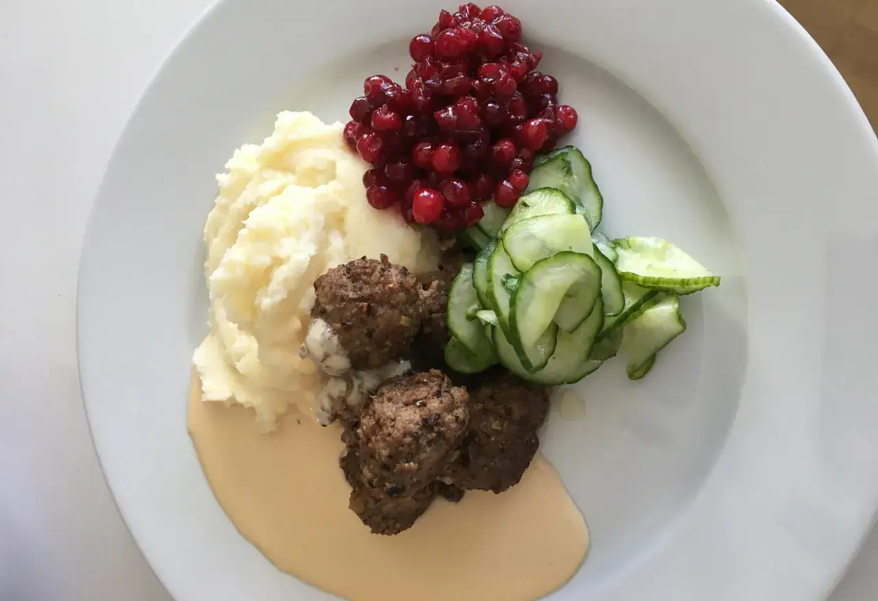 En tallrik med k&ouml;ttbullar, kr&auml;migt potatismos, skivad gurka och r&aring;r&ouml;rda lingon. Potatisbullarna av potatismos ser fluffiga ut.