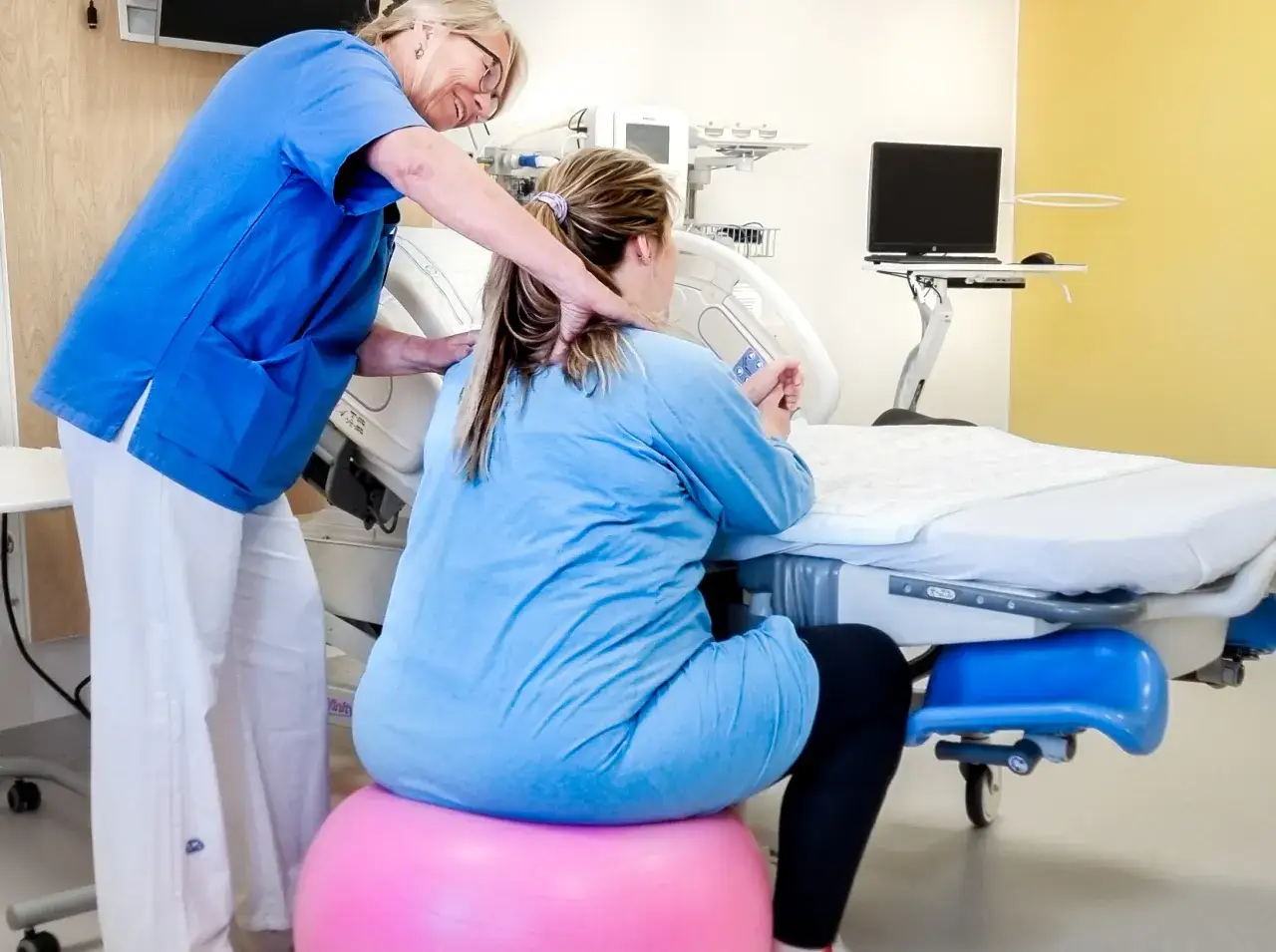 Barnmorska ger st&ouml;d till en kvinna i gravid vecka 36 som sitter p&aring; en tr&auml;ningsboll vid en f&ouml;rlossningss&auml;ng.