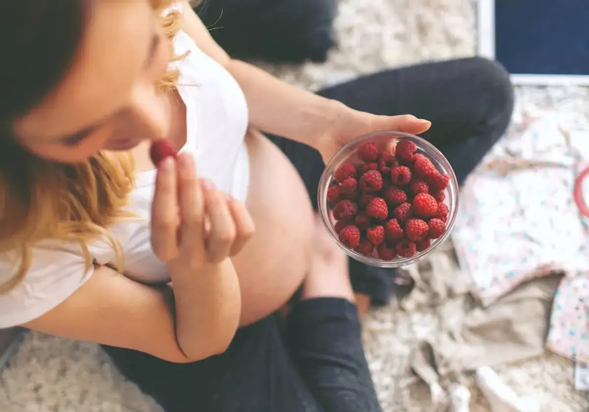 Gravid kvinna &auml;ter hallon fr&aring;n en sk&aring;l. Hon verkar njuta av sin r&aring;biff-liknande frukost.