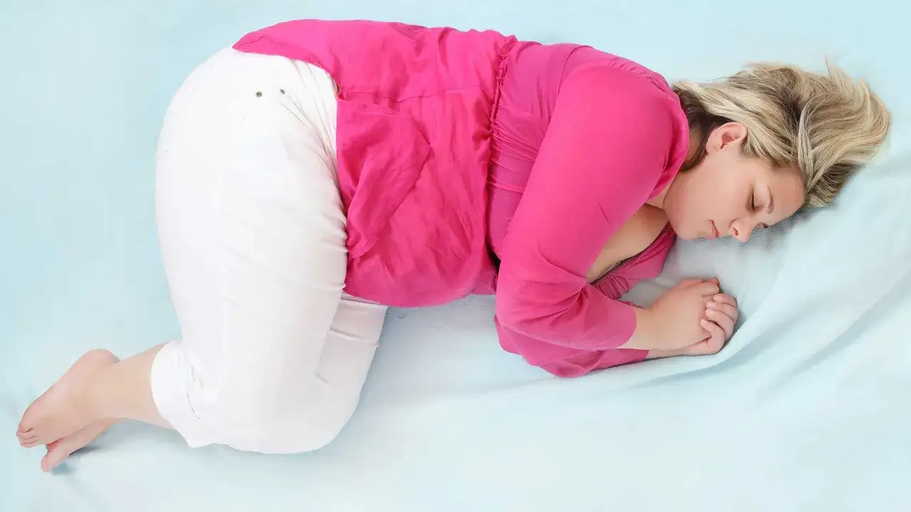En kvinna i rosa tr&ouml;ja och vita byxor sover i fosterst&auml;llning. V 34.