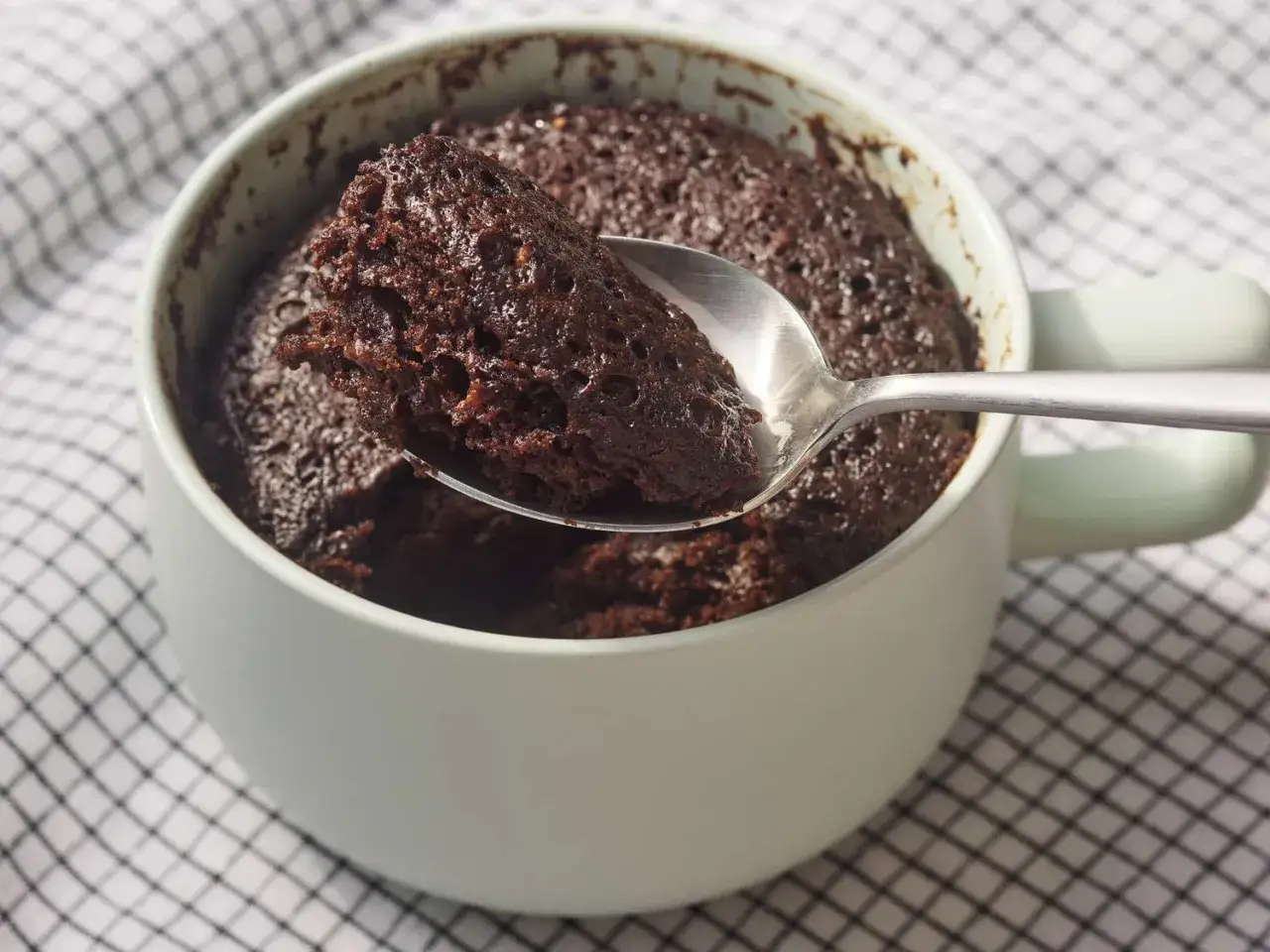 En sked tar en bit av en m&ouml;rk, saftig chokladkaka i en mugg. En perfekt nyttig mugcake f&ouml;r en snabb fika.