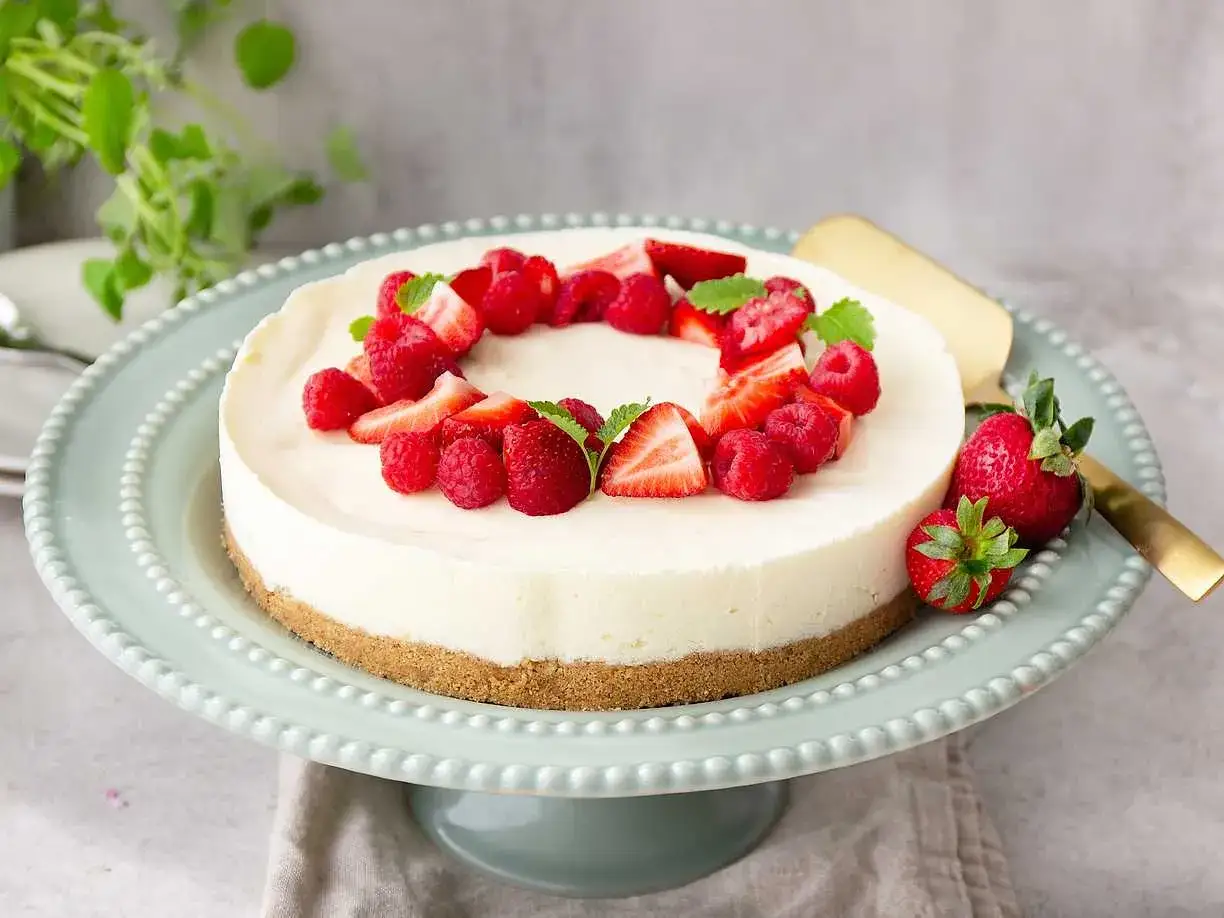 En vacker, nyttig cheesecake dekorerad med f&auml;rska hallon och jordgubbar, serverad p&aring; ett ljusgr&ouml;nt t&aring;rtfat.