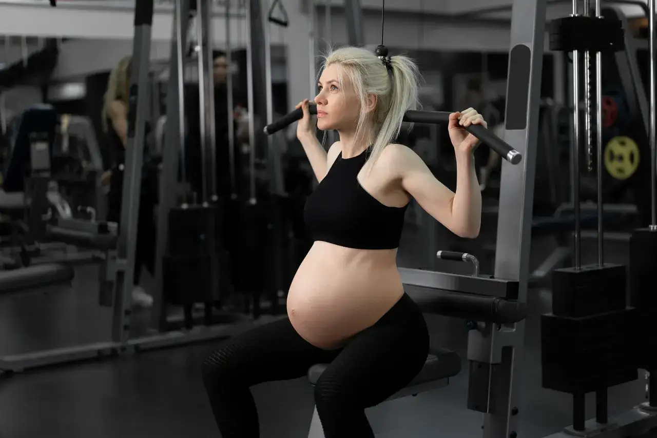 Gravid kvinna lyfter tungt i gym. Hon tränar ryggen med en kabelmaskin, stark och fokuserad.