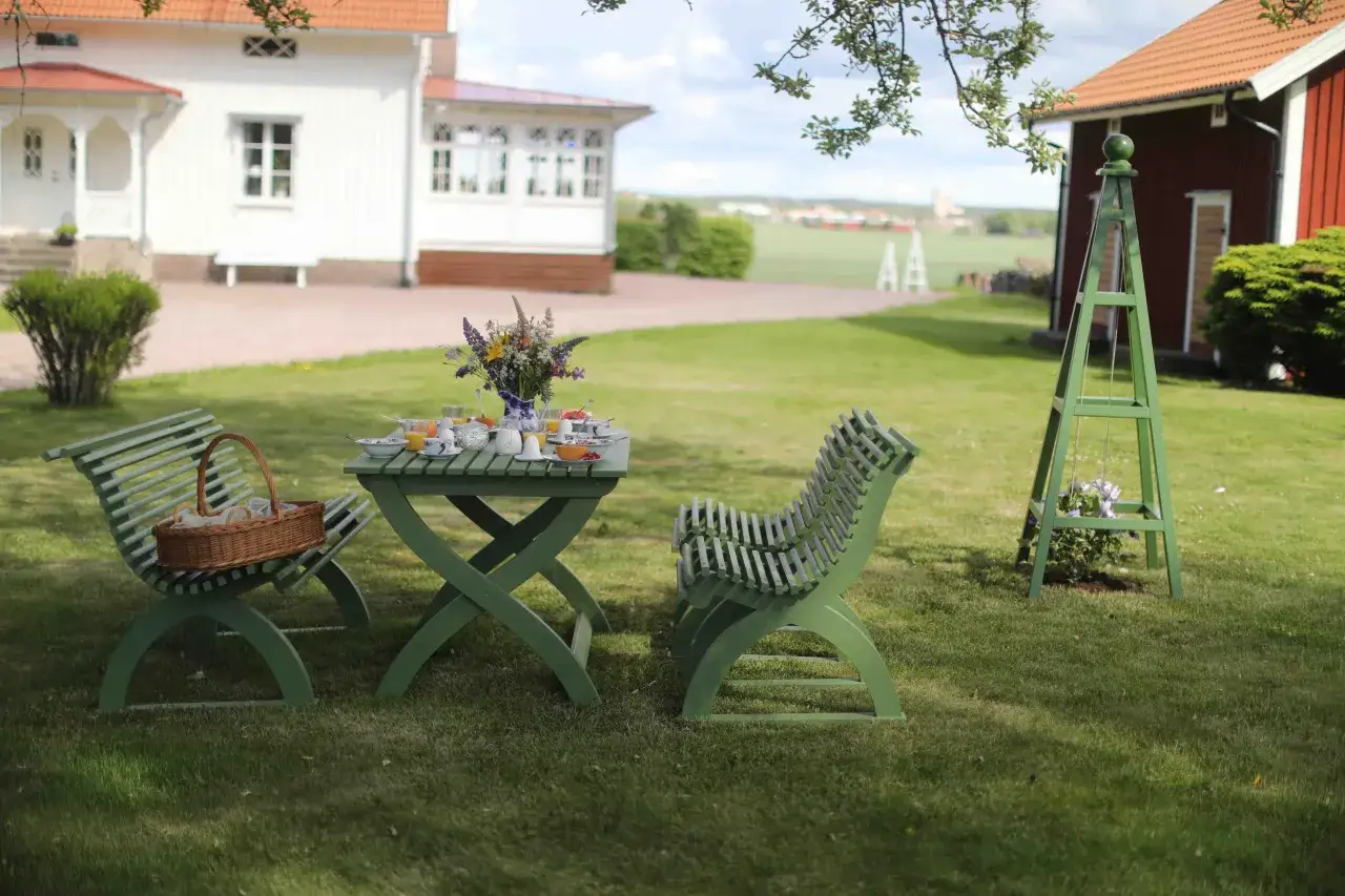 En gr&ouml;n rosentorn ritning st&aring;r i en tr&auml;dg&aring;rd med ett frukostbord uppdukat.