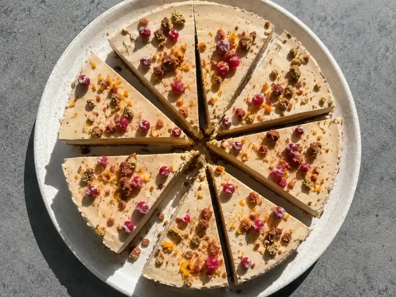 En skivad cheesecake med pepparkaksbotten, toppad med r&ouml;da b&auml;r och smulor.