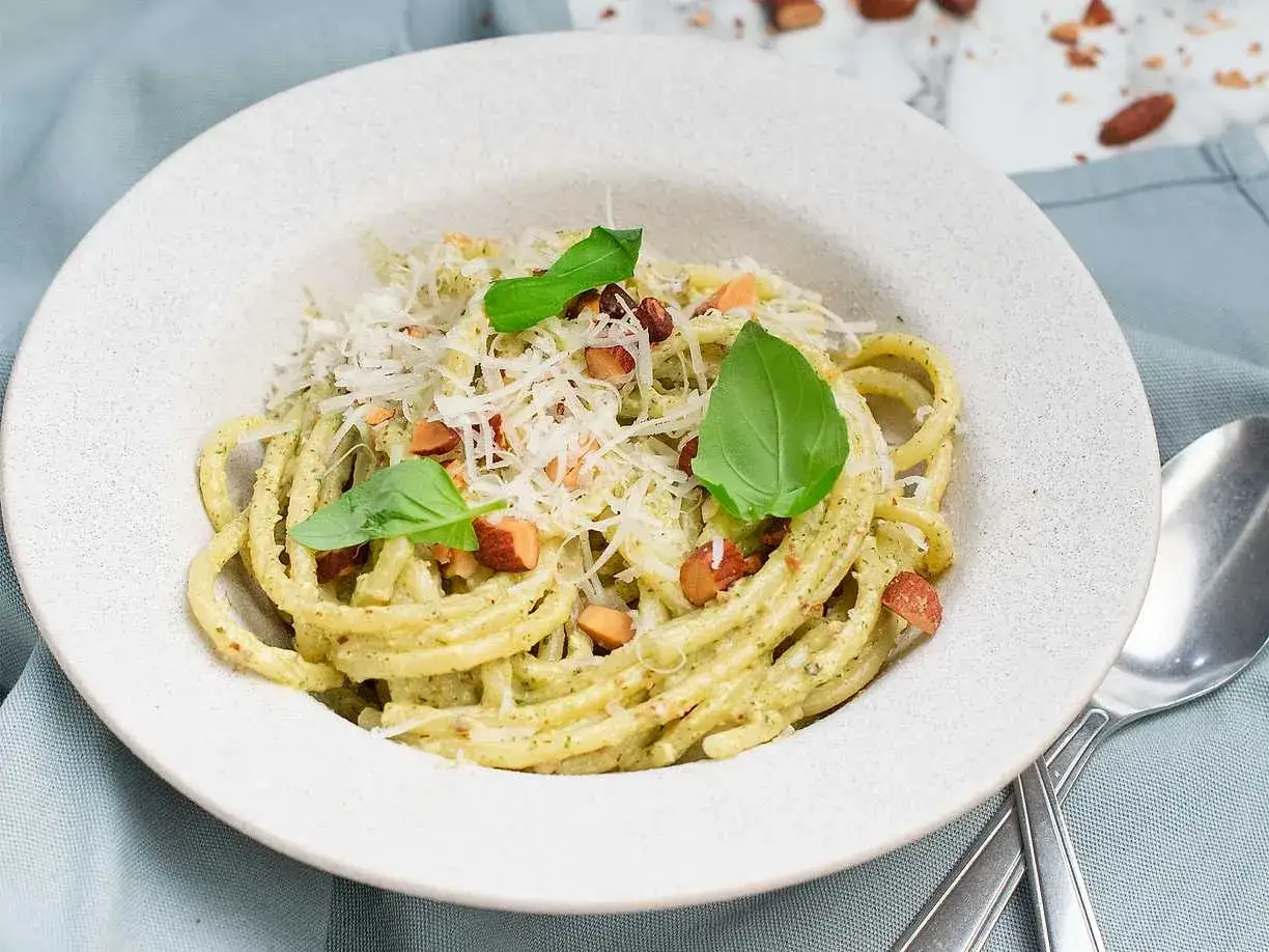 En portion kr&auml;mig pasta med pesto, toppad med riven ost, n&ouml;tter och basilika. Perfekt spagetti koktid f&ouml;r en snabb och god m&aring;ltid.