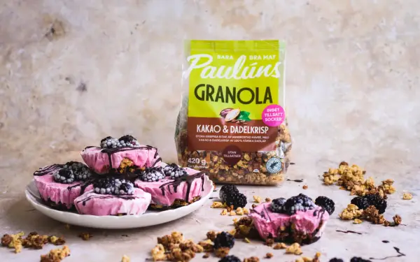 Rosa yoghurtglass med bär och granola, perfekt för ett snabbt yoghurtglass recept. Paulúns granola i bakgrunden.