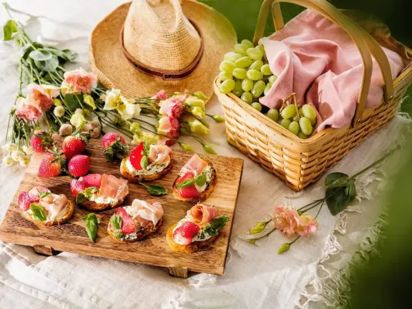 En härlig picknick med bruschetta toppad med jordgubbar och parmaskinka, färska vindruvor i korg och blommor.