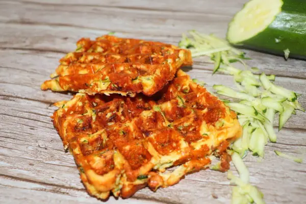 Gyldene zucchini våfflor, perfekt stekta, med riven zucchini och en hel zucchini i bakgrunden.